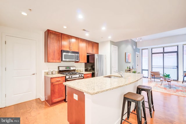 kitchen with appliances with stainless steel finishes, a center island with sink, a kitchen breakfast bar, light hardwood / wood-style floors, and sink