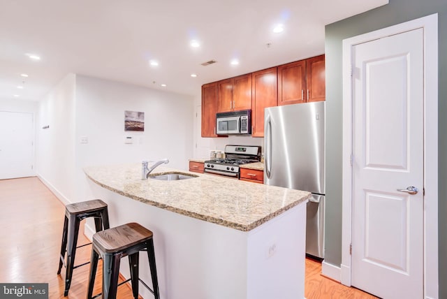 kitchen featuring a center island with sink, light hardwood / wood-style flooring, appliances with stainless steel finishes, sink, and light stone countertops