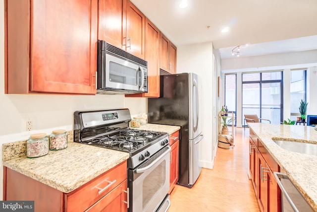 kitchen with sink, stainless steel appliances, light stone counters, and light hardwood / wood-style flooring