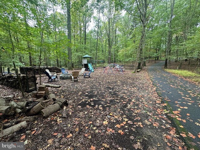 view of yard with a playground, a fire pit, and a wooded view