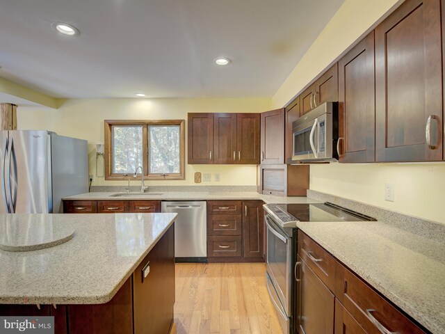 kitchen featuring light stone countertops, recessed lighting, light wood-style flooring, stainless steel appliances, and a sink