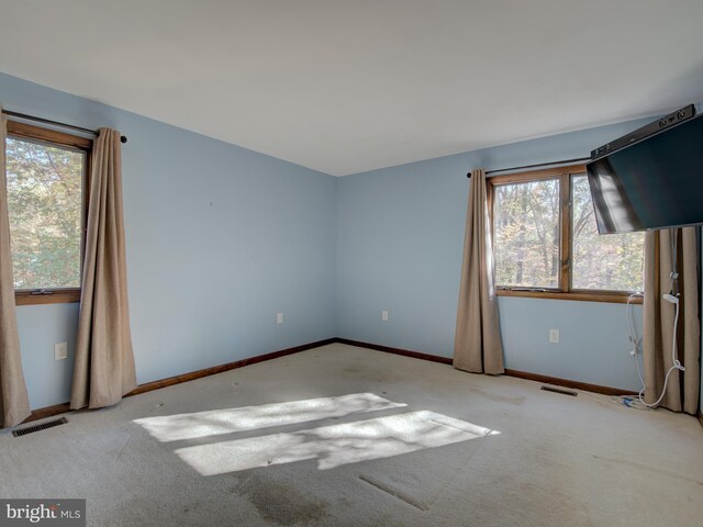 carpeted empty room featuring plenty of natural light, baseboards, and visible vents