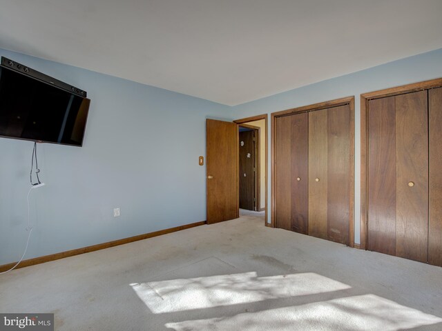 unfurnished bedroom featuring carpet flooring, baseboards, and multiple closets