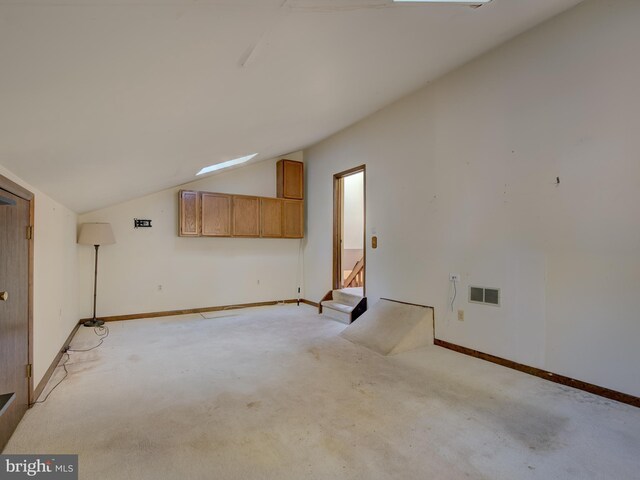 empty room featuring visible vents, light colored carpet, baseboards, and lofted ceiling