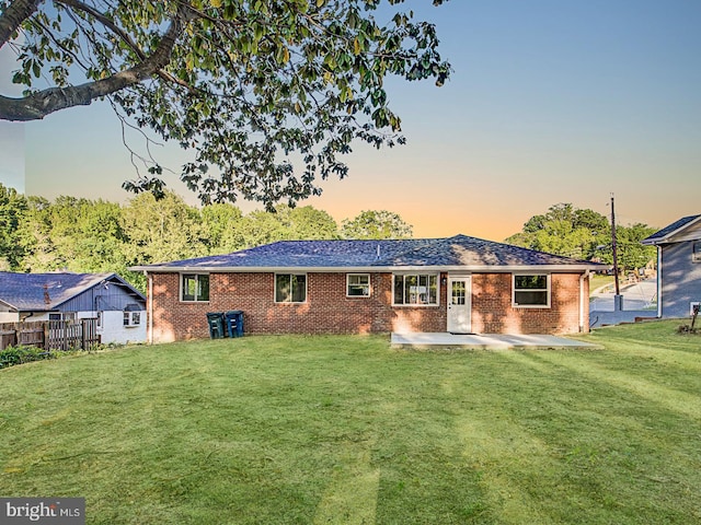 back house at dusk featuring a yard and a patio