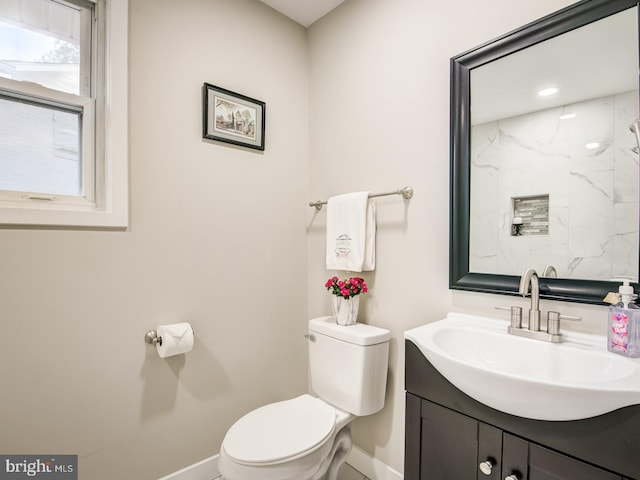 bathroom with a tile shower, vanity, and toilet