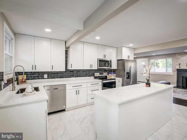 kitchen with a center island, sink, white cabinetry, a fireplace, and appliances with stainless steel finishes