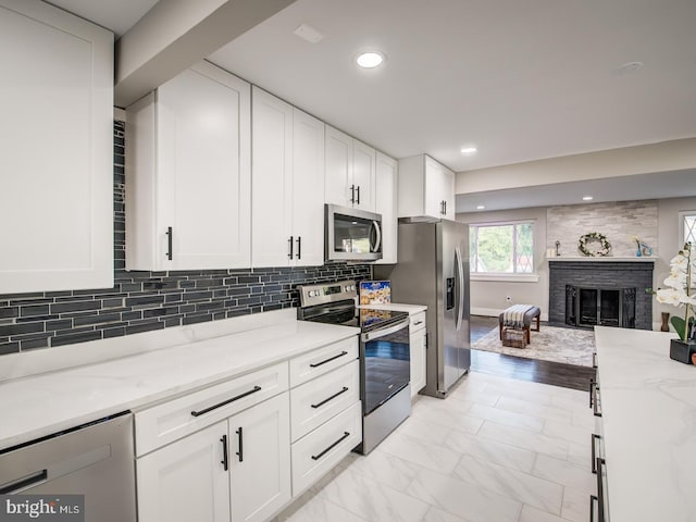 kitchen featuring white cabinetry, a brick fireplace, backsplash, light stone countertops, and stainless steel appliances