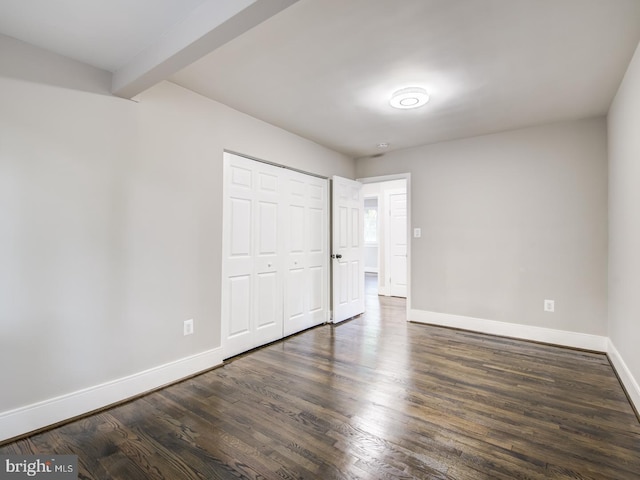 unfurnished bedroom featuring beam ceiling, dark wood-type flooring, and a closet