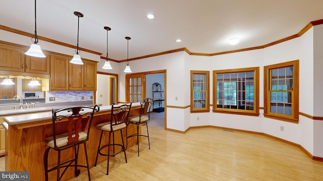 kitchen featuring pendant lighting, sink, ornamental molding, a kitchen island, and light wood-type flooring