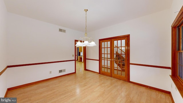 spare room with an inviting chandelier, light hardwood / wood-style floors, and french doors