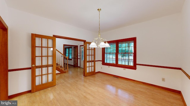 empty room with wood-type flooring and a notable chandelier