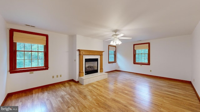 unfurnished living room with light hardwood / wood-style flooring, a wealth of natural light, a premium fireplace, and ceiling fan