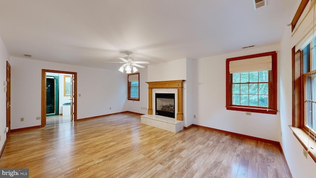 unfurnished living room featuring a premium fireplace, light wood-type flooring, ceiling fan, and a healthy amount of sunlight