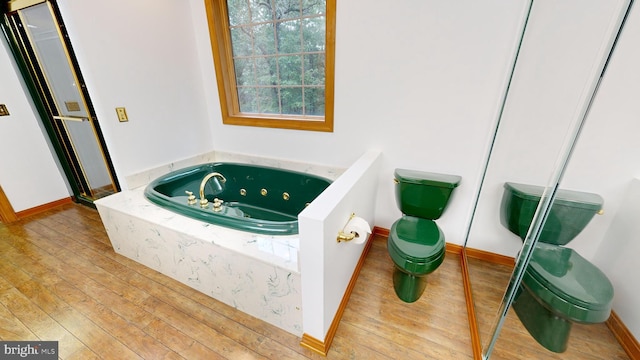 bathroom featuring a relaxing tiled tub, hardwood / wood-style floors, and toilet