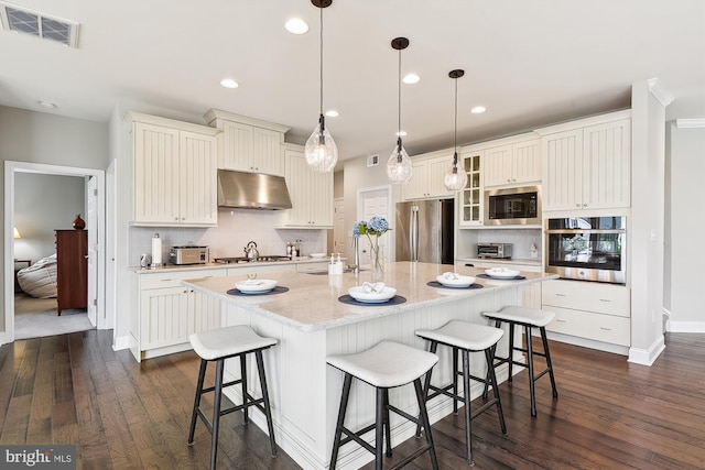 kitchen with pendant lighting, an island with sink, appliances with stainless steel finishes, and dark hardwood / wood-style flooring