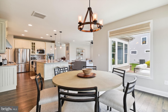 dining room with ceiling fan with notable chandelier, sink, and dark hardwood / wood-style flooring