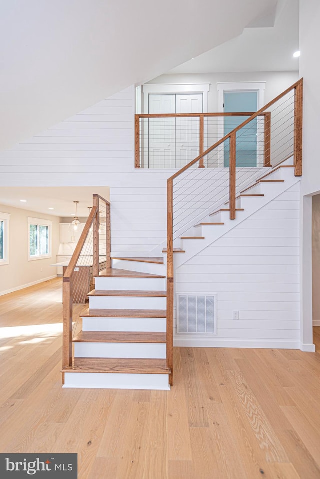 stairway with high vaulted ceiling, wood walls, and hardwood / wood-style floors