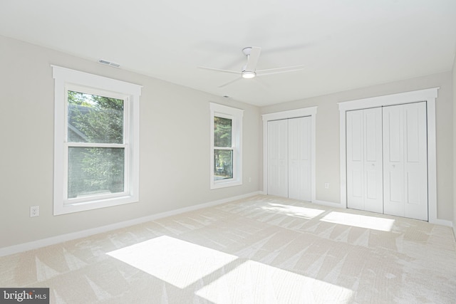 unfurnished bedroom with ceiling fan, two closets, and light colored carpet