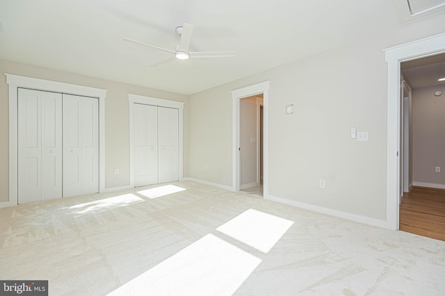 unfurnished bedroom featuring two closets, light colored carpet, and ceiling fan