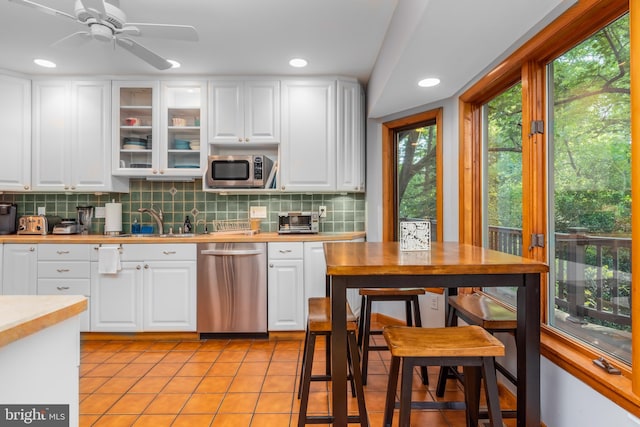 kitchen featuring appliances with stainless steel finishes, light tile patterned flooring, white cabinets, backsplash, and sink