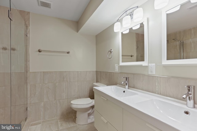 bathroom with vanity, toilet, tiled shower, and tile walls