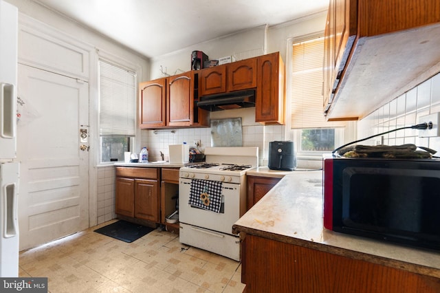 kitchen featuring backsplash, ornamental molding, sink, and white gas stove