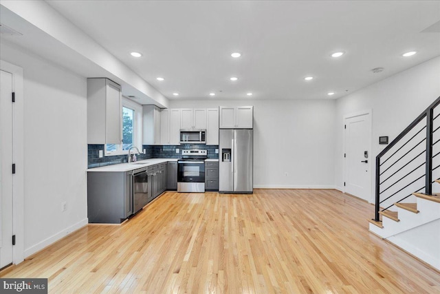 kitchen with white cabinets, decorative backsplash, appliances with stainless steel finishes, light hardwood / wood-style flooring, and sink