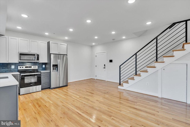 kitchen with decorative backsplash, white cabinets, stainless steel appliances, and light wood-type flooring