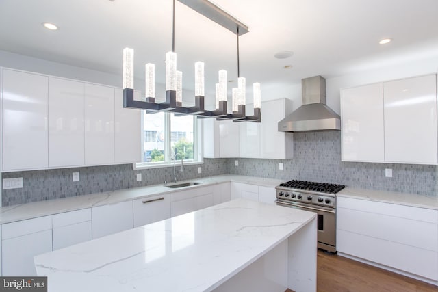 kitchen with decorative light fixtures, wall chimney range hood, high end stainless steel range, and white cabinets