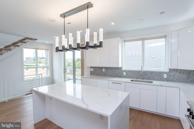 kitchen featuring white cabinets, decorative light fixtures, sink, and light hardwood / wood-style flooring