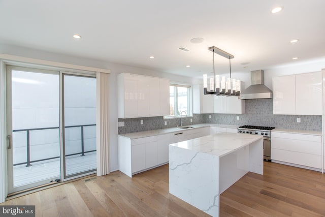 kitchen with stainless steel stove, wall chimney exhaust hood, white cabinetry, and a kitchen island