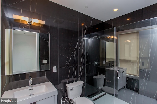 bathroom with vanity, tile walls, toilet, and a shower with door