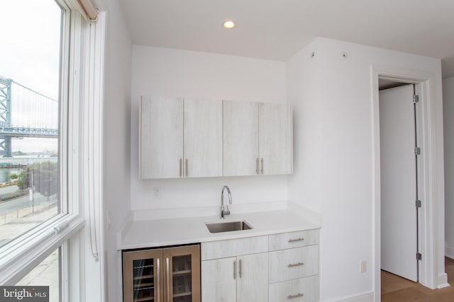 bar featuring light brown cabinets, light hardwood / wood-style floors, sink, and wine cooler