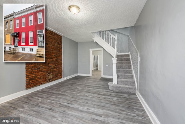 interior space featuring a textured ceiling, brick wall, and hardwood / wood-style flooring