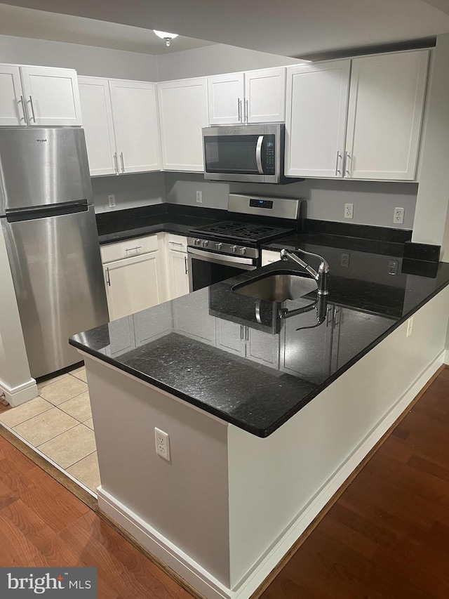 kitchen with light hardwood / wood-style floors, white cabinetry, kitchen peninsula, appliances with stainless steel finishes, and dark stone counters