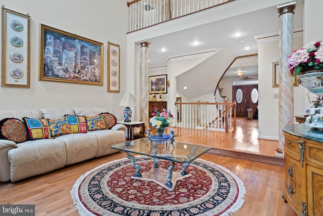 living room with decorative columns, light hardwood / wood-style floors, crown molding, and a high ceiling