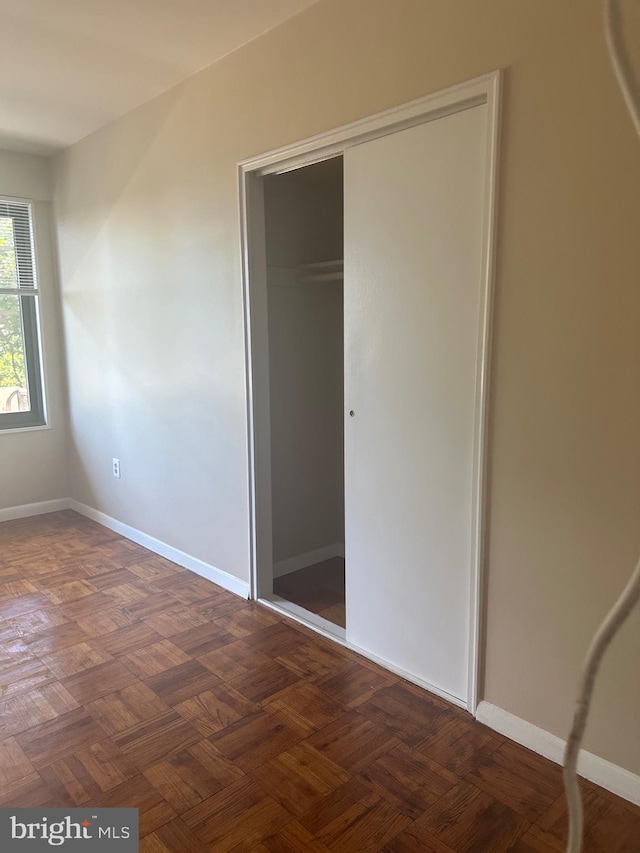 unfurnished bedroom featuring dark parquet floors and a closet