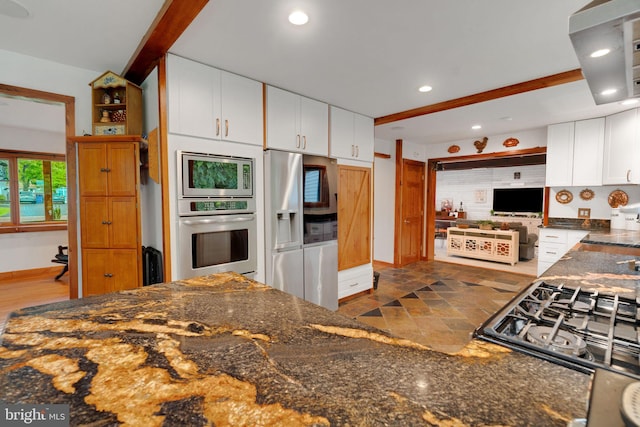 kitchen with dark stone counters, white cabinets, beam ceiling, and appliances with stainless steel finishes