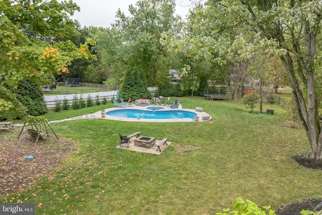 view of pool with a lawn, a trampoline, and a fire pit