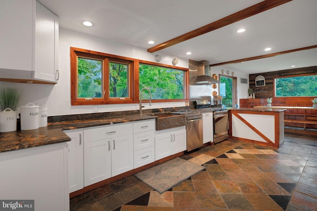 kitchen with a healthy amount of sunlight, wall chimney range hood, and white cabinets