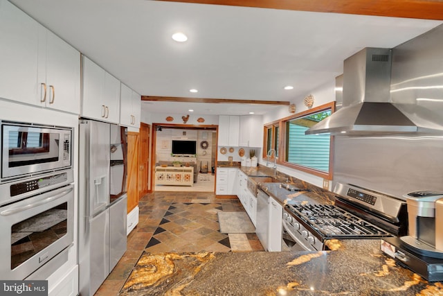 kitchen with sink, island exhaust hood, white cabinetry, appliances with stainless steel finishes, and dark stone counters