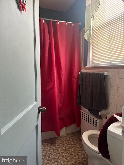 bathroom with a shower with shower curtain, tile walls, radiator, and toilet