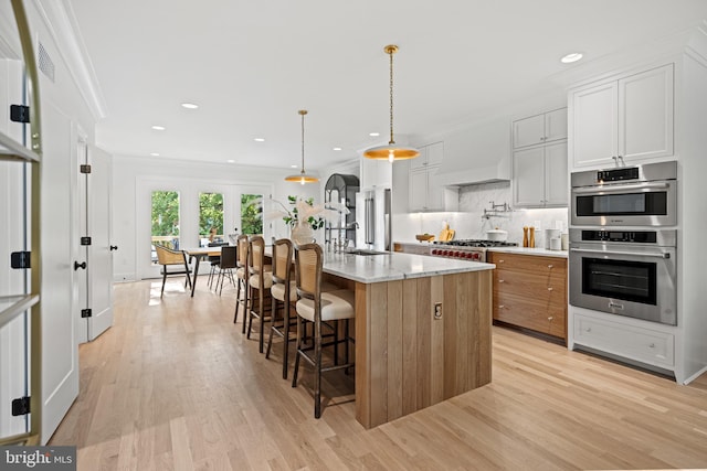 kitchen with stainless steel appliances, light hardwood / wood-style flooring, an island with sink, decorative light fixtures, and white cabinets