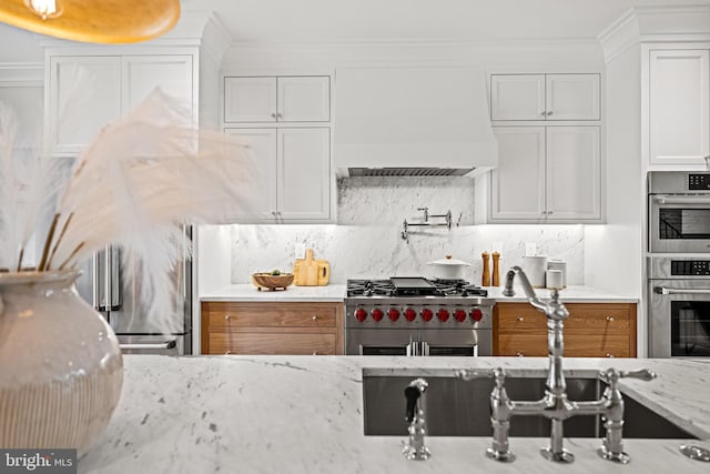 kitchen featuring white cabinets, stainless steel appliances, light stone countertops, and premium range hood