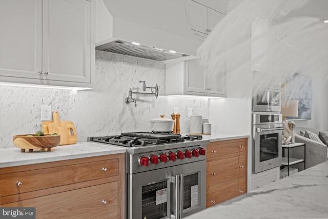 kitchen with light stone countertops, white cabinetry, stainless steel appliances, and custom range hood