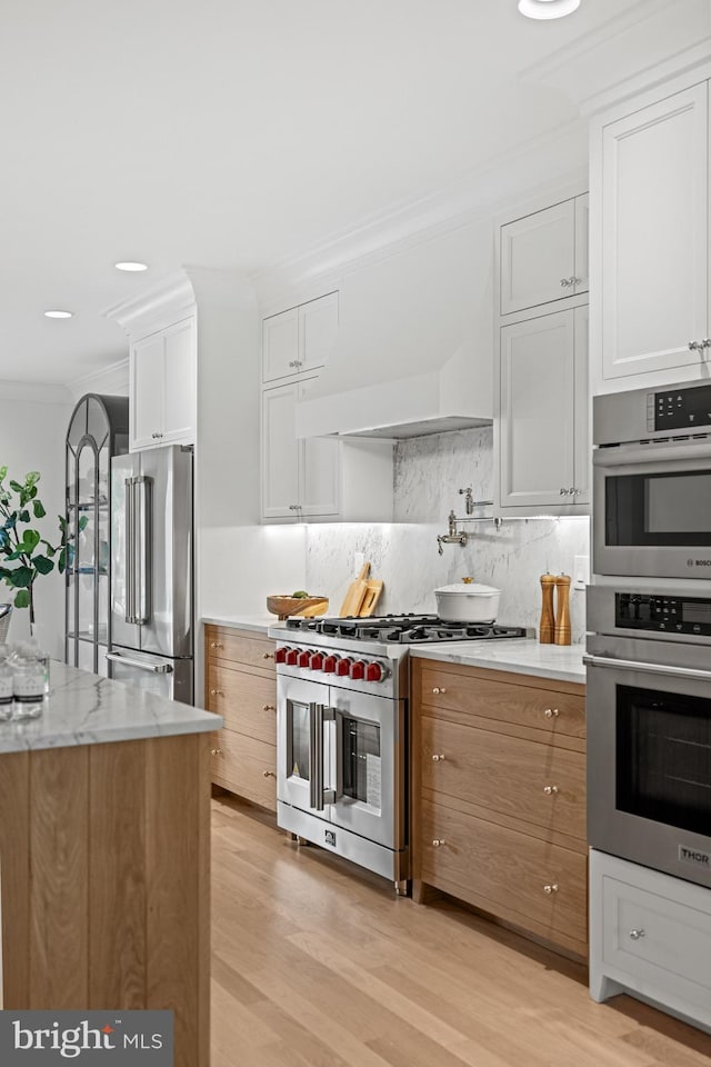 kitchen featuring light stone counters, light hardwood / wood-style flooring, white cabinets, and premium appliances