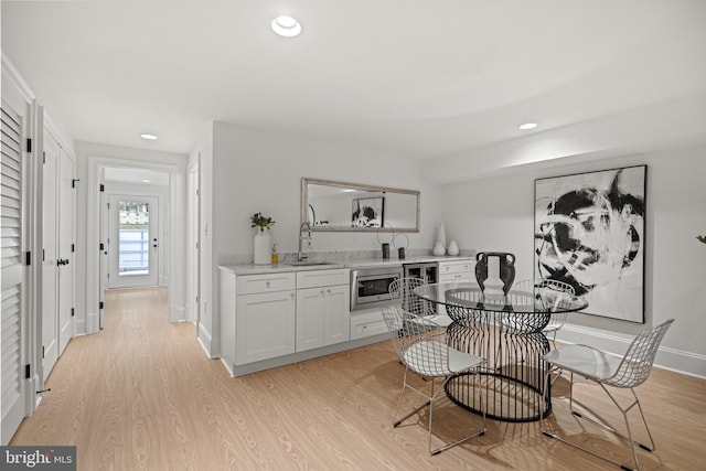 kitchen with sink, stainless steel microwave, wine cooler, light hardwood / wood-style flooring, and white cabinets