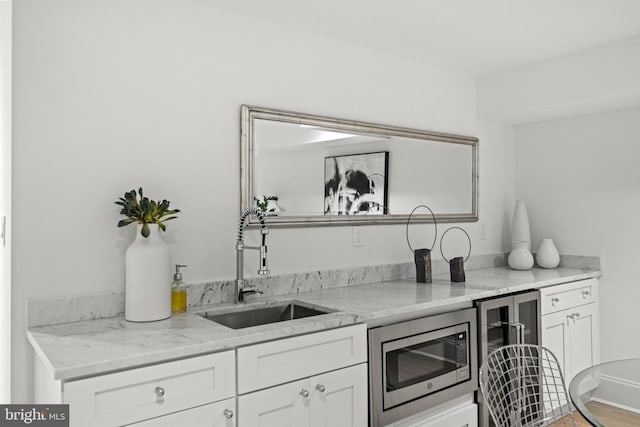 kitchen featuring white cabinetry, light stone counters, stainless steel microwave, and sink