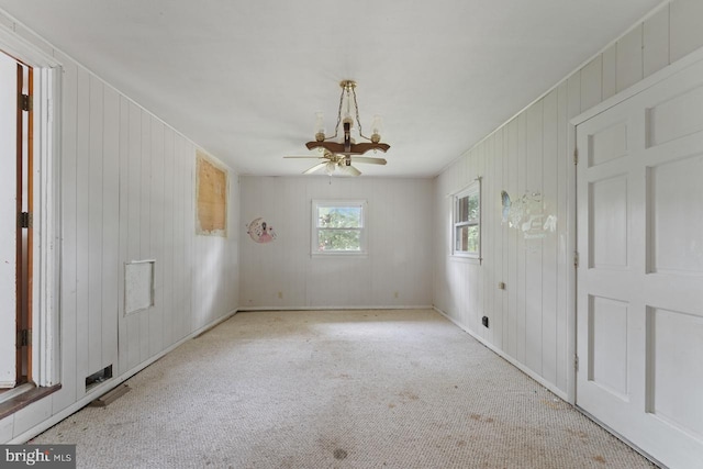 spare room with light colored carpet, ceiling fan with notable chandelier, and wooden walls